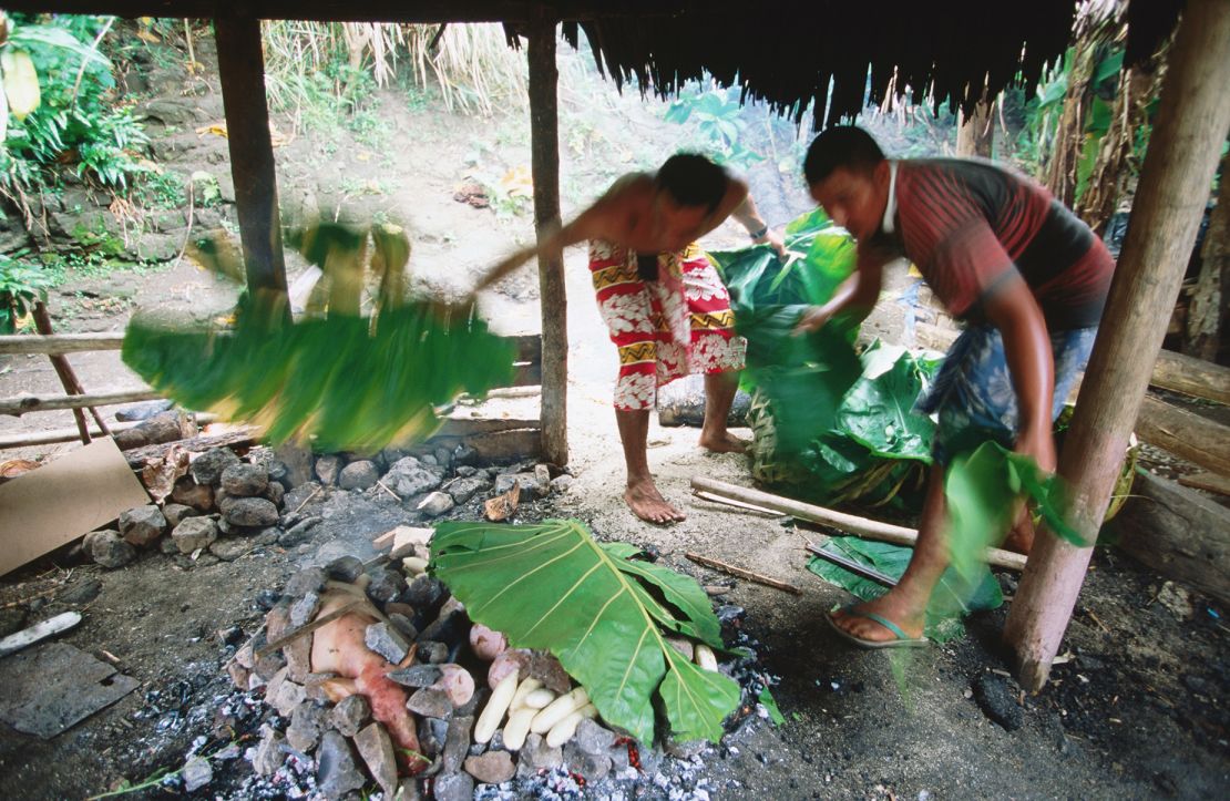 Men cover the umu, Samoa's version of the barbecue, with leaves.